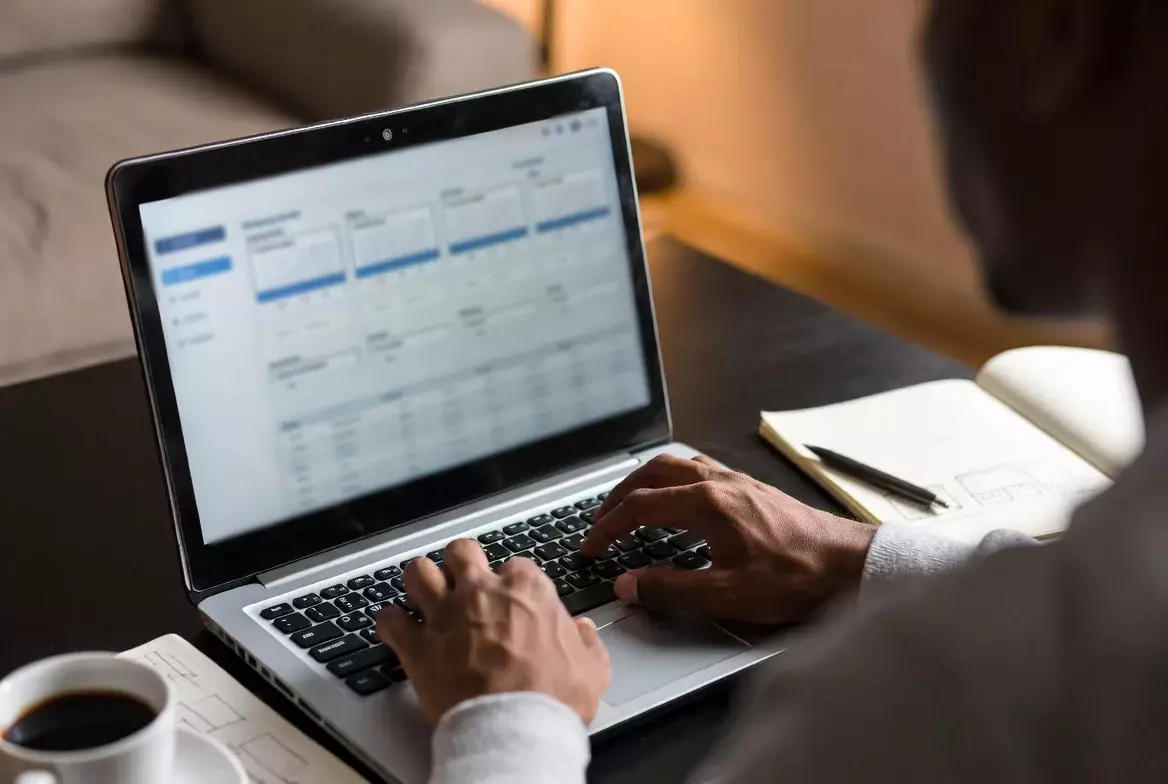 Person analysiert Fußballstatistiken auf Laptop mit Notizen und Diagrammen