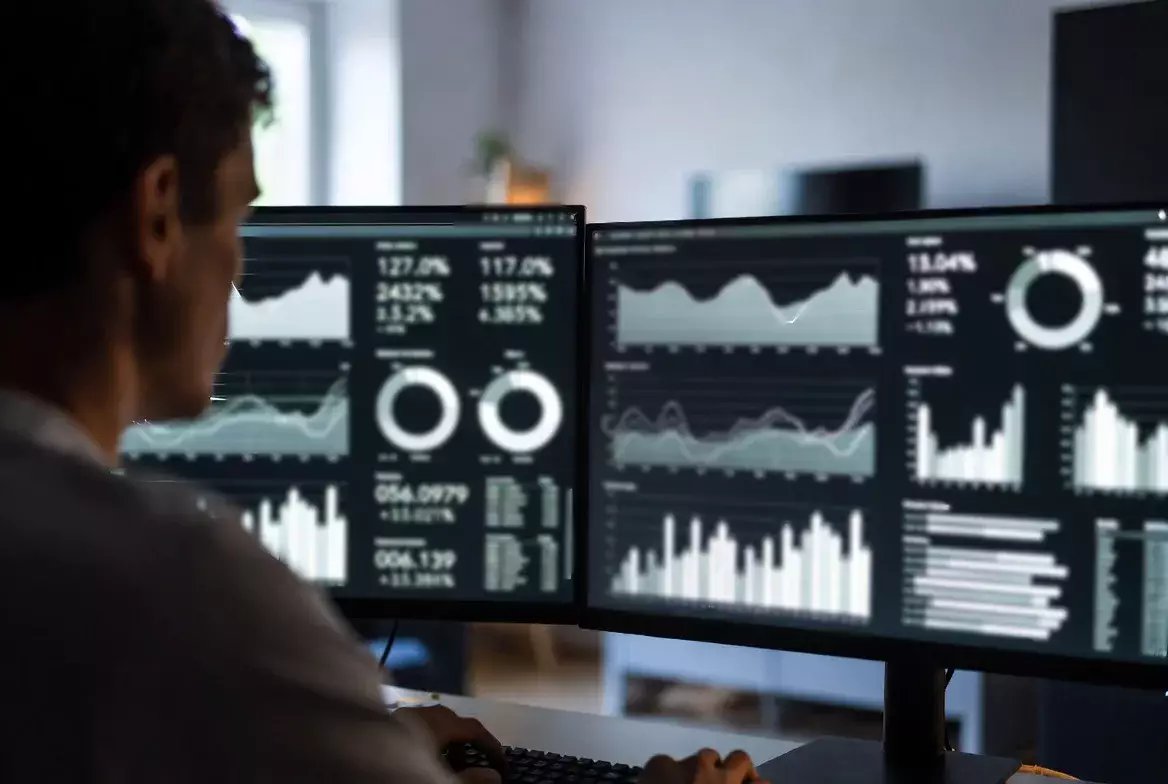 Person vergleicht verschiedene Datenquellen auf zwei Bildschirmen
